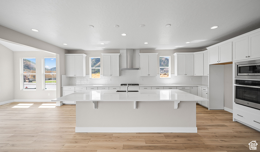 Kitchen featuring wall chimney exhaust hood, appliances with stainless steel finishes, recessed lighting, a breakfast bar area, and light countertops