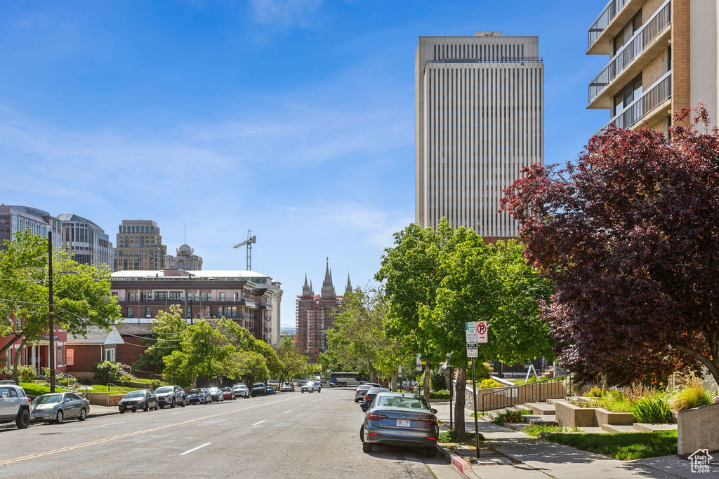 View of asphalt street featuring sidewalks, a city view, curbs, and street lighting