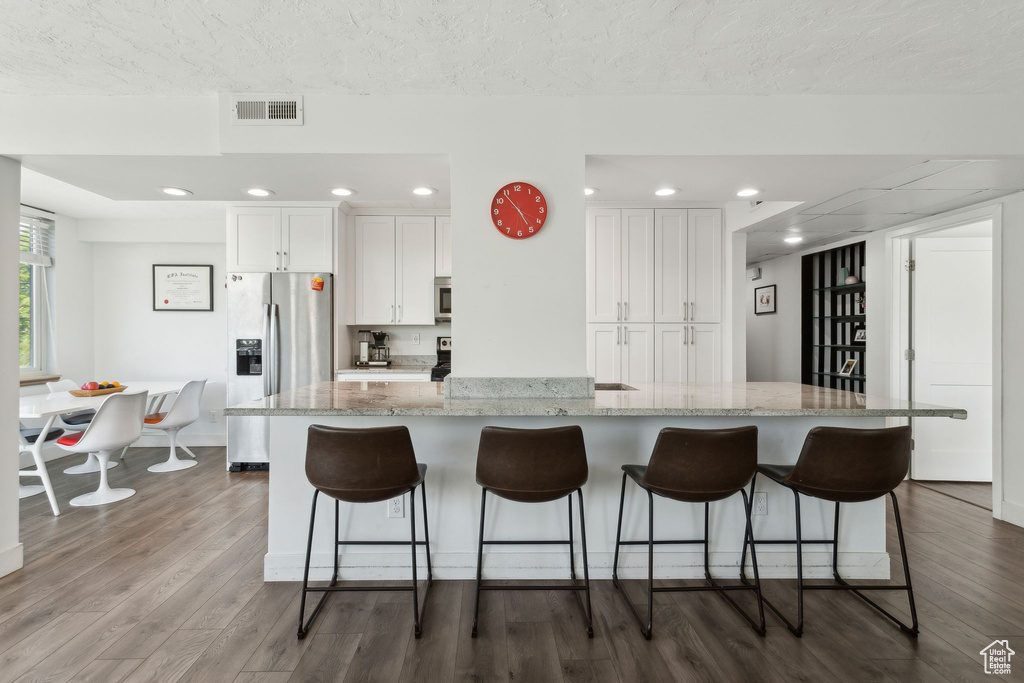 Kitchen with appliances with stainless steel finishes, white cabinetry, dark wood-type flooring, a kitchen bar, and recessed lighting