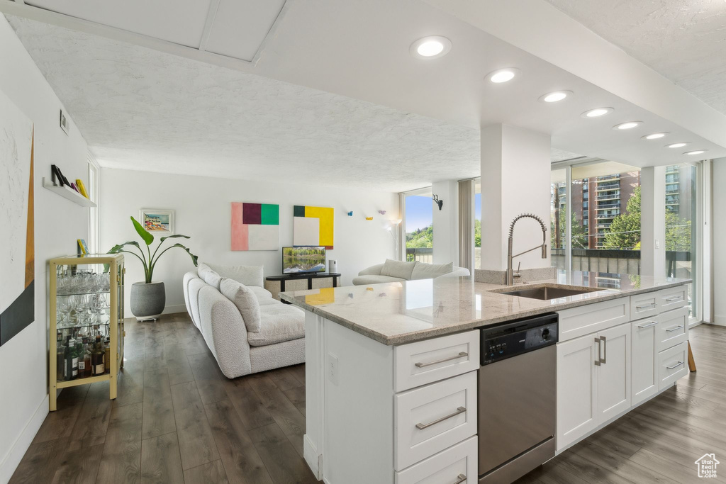 Kitchen featuring stainless steel dishwasher, a sink, open floor plan, baseboards, and light stone counters
