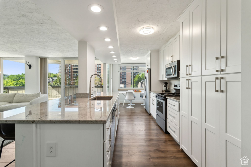 Kitchen featuring appliances with stainless steel finishes, a sink, a textured ceiling, a center island with sink, and open floor plan