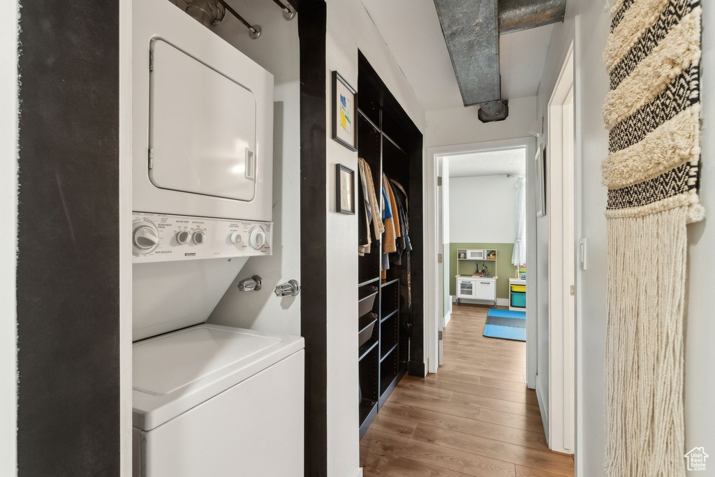Laundry area with stacked washer and clothes dryer and wood finished floors