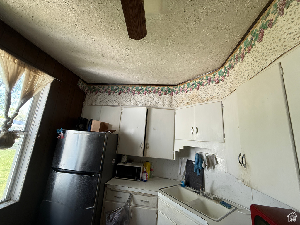 Kitchen with a textured ceiling, freestanding refrigerator, light countertops, white cabinets, and a sink