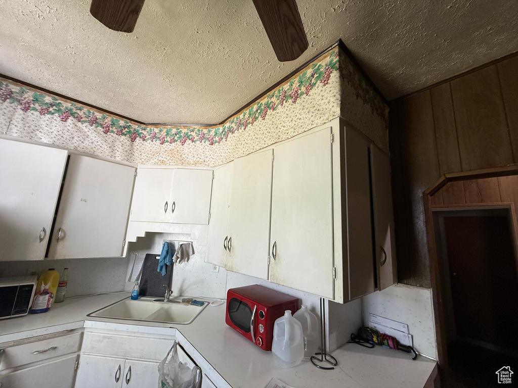 Kitchen featuring light countertops, a textured ceiling, a sink, white cabinets, and a ceiling fan