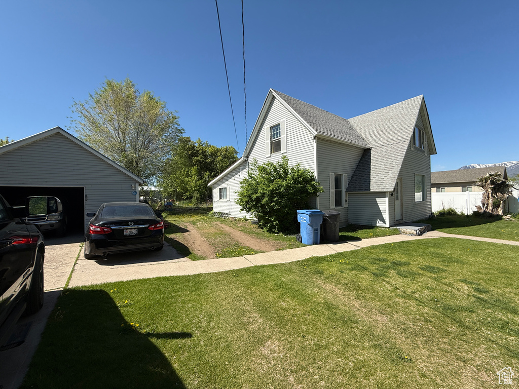 View of side of property featuring a shingled roof, a yard, and a garage