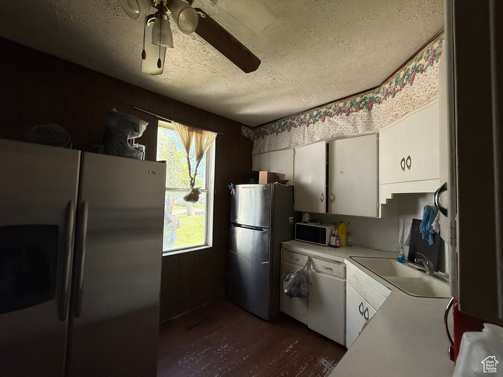 Kitchen featuring stainless steel refrigerator with ice dispenser, freestanding refrigerator, a textured ceiling, dark wood-style flooring, and white cabinets
