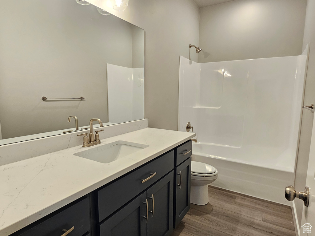 Bathroom featuring wood finished floors, vanity, toilet, and tub / shower combination