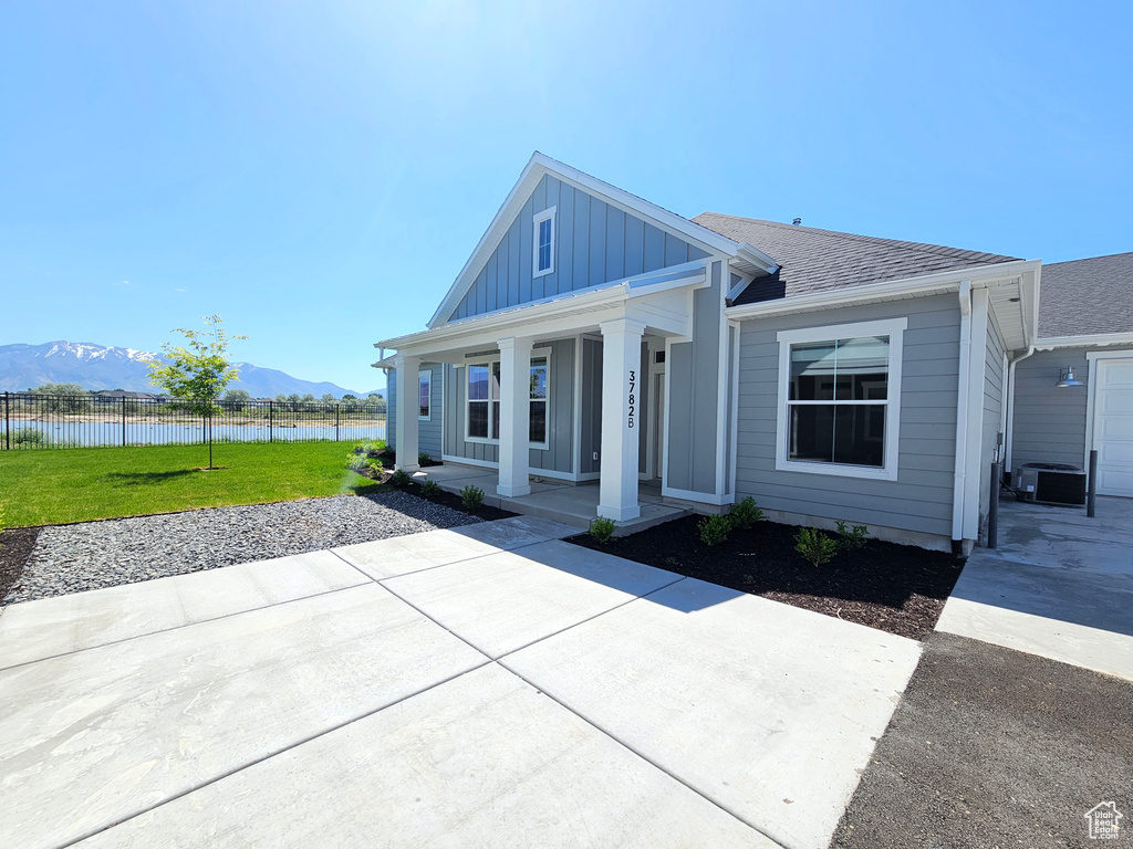 View of front of house featuring a water and mountain view, board and batten siding, covered porch, central AC, and a shingled roof