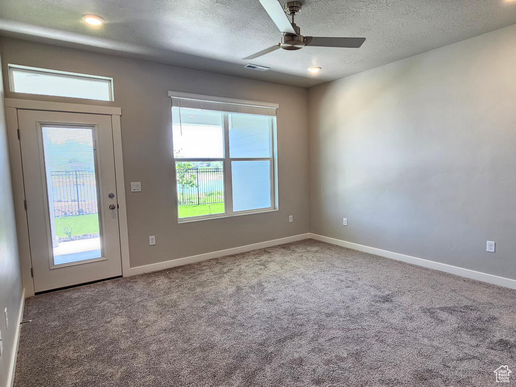 Carpeted spare room with ceiling fan, baseboards, and a textured ceiling
