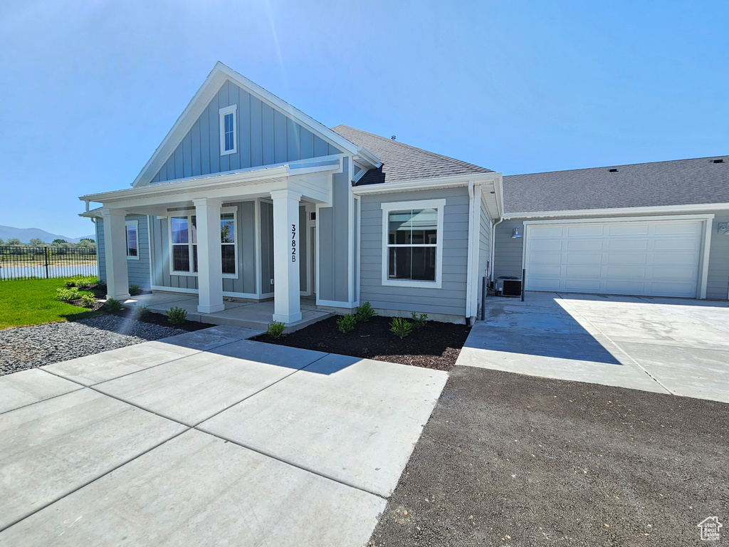View of front of property featuring board and batten siding, concrete driveway, a porch, fence, and a water view