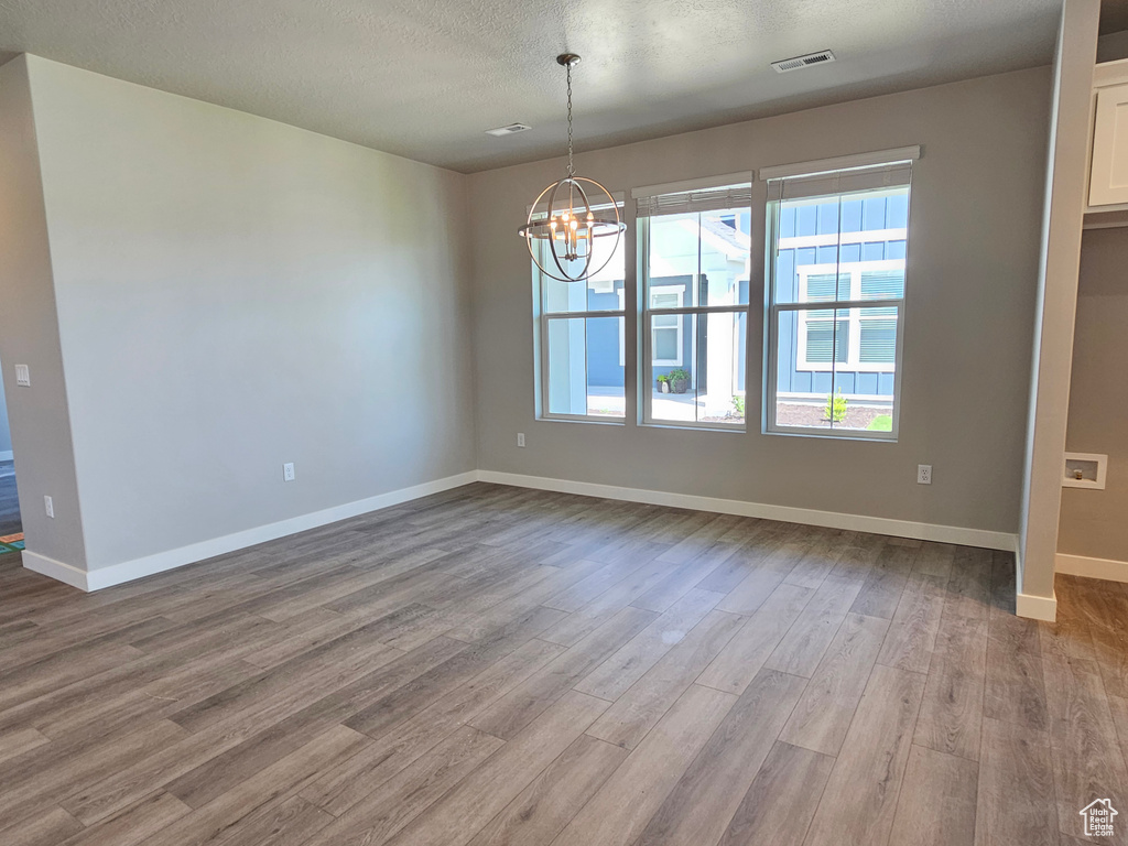 Spare room featuring wood finished floors, a chandelier, plenty of natural light, baseboards, and a textured ceiling