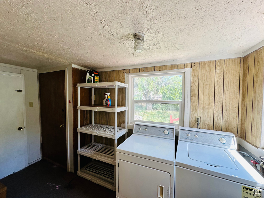 Laundry room featuring washing machine and clothes dryer, a textured ceiling, and wood walls