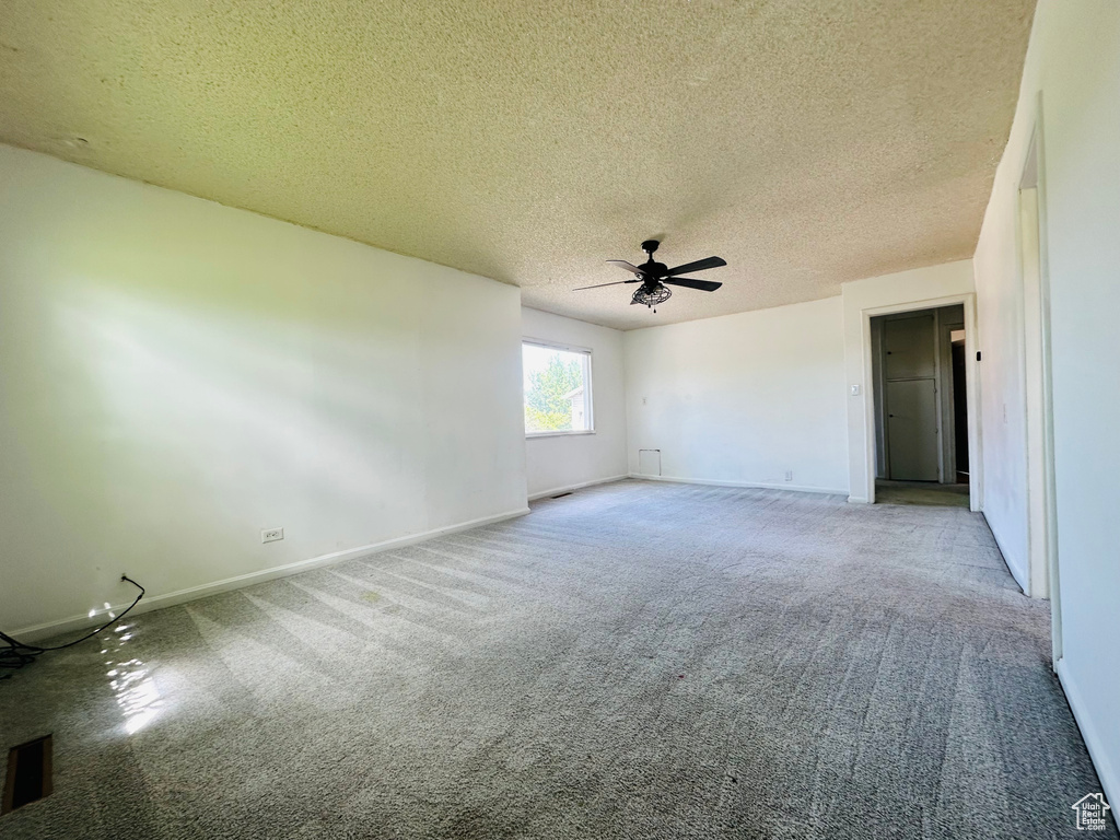 Carpeted empty room with ceiling fan, baseboards, and a textured ceiling