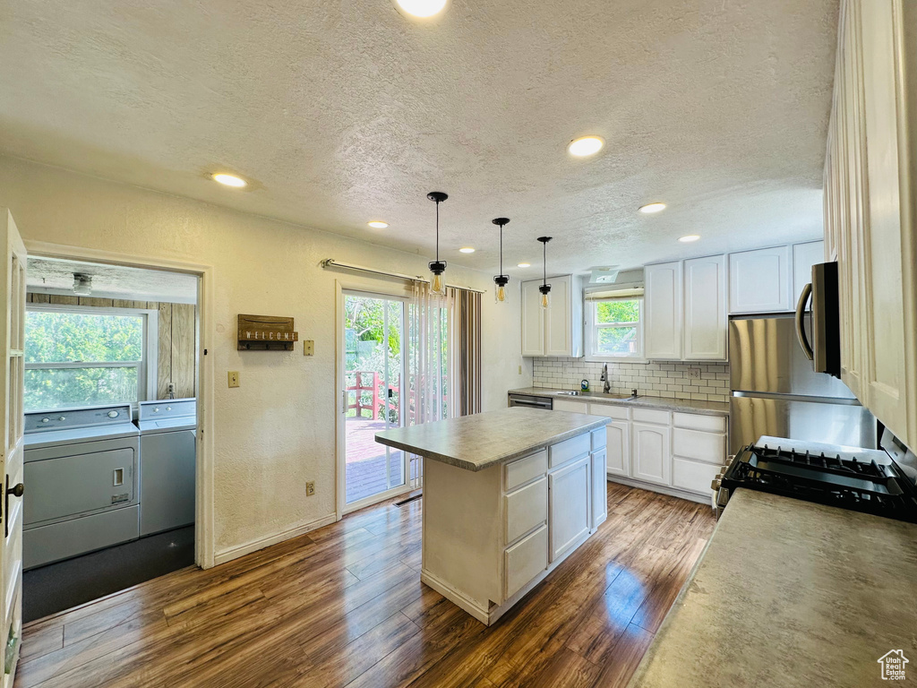 Kitchen with independent washer and dryer, gas range, a textured ceiling, dark wood finished floors, and a kitchen island