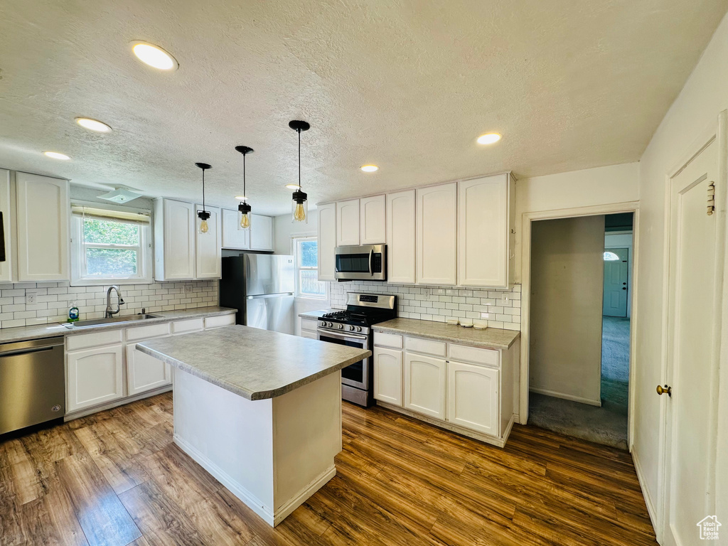 Kitchen with appliances with stainless steel finishes, a sink, tasteful backsplash, white cabinets, and a textured ceiling
