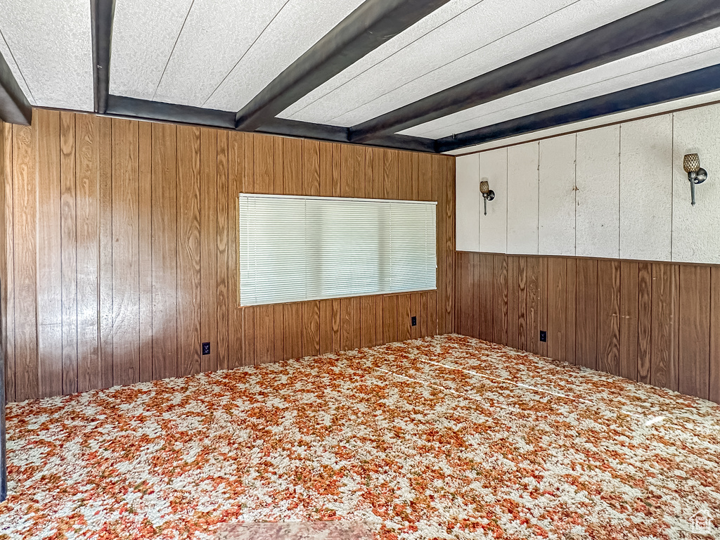Unfurnished bedroom with wood walls, carpet flooring, and beam ceiling