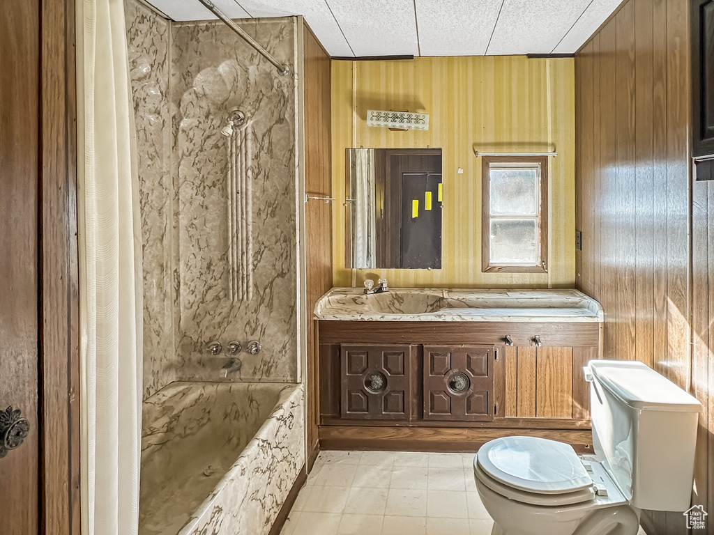 Full bath featuring toilet, shower / bath combination with curtain, wooden walls, and vanity