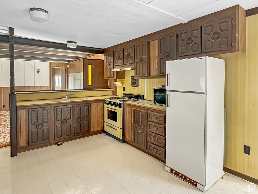 Kitchen with white appliances, a sink, under cabinet range hood, light countertops, and light flooring
