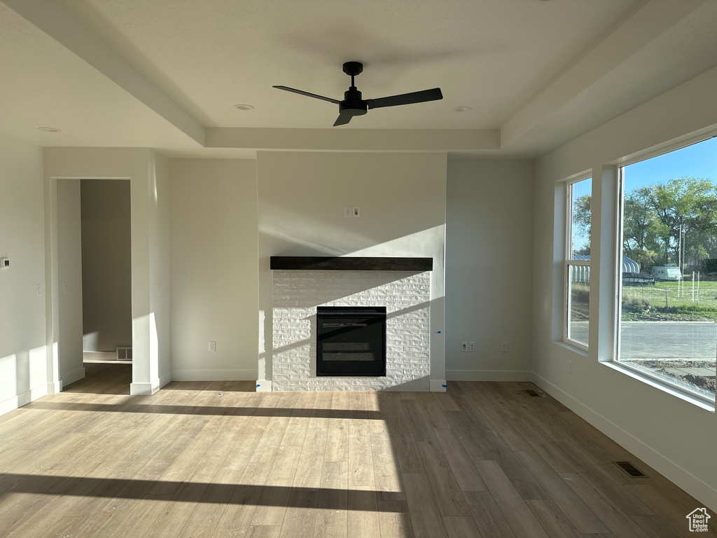 Unfurnished living room featuring a ceiling fan, wood finished floors, baseboards, and a raised ceiling