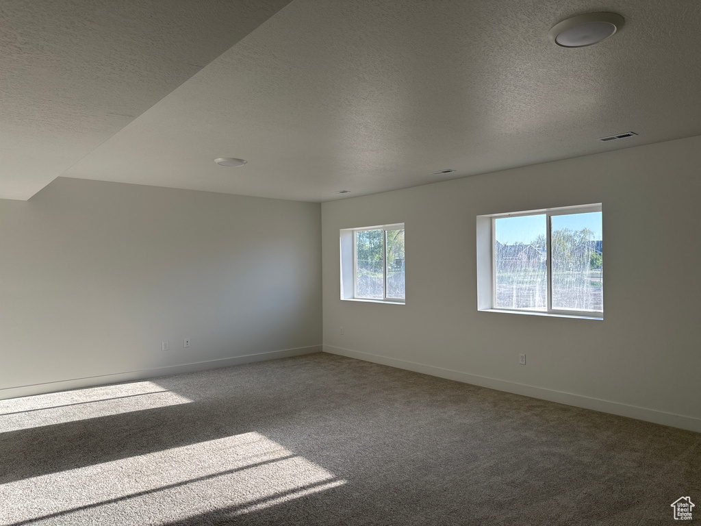 Spare room featuring a textured ceiling, carpet floors, and baseboards