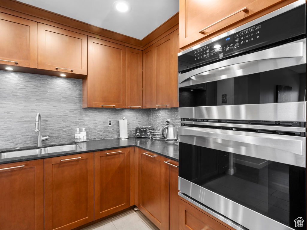 Kitchen with a sink, stainless steel double oven, decorative backsplash, and brown cabinetry