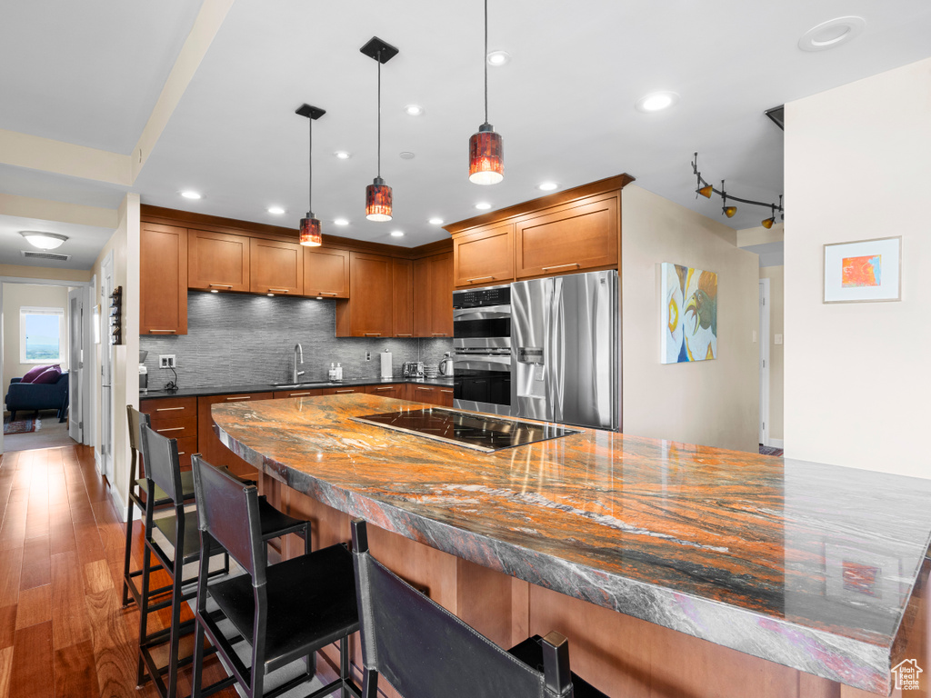 Kitchen featuring stainless steel appliances, dark countertops, brown cabinetry, a kitchen breakfast bar, and a sink