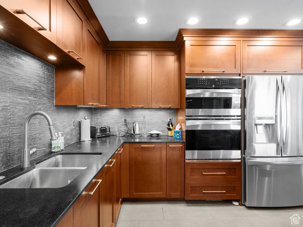 Kitchen with stainless steel appliances, a sink, light tile patterned floors, dark stone counters, and tasteful backsplash