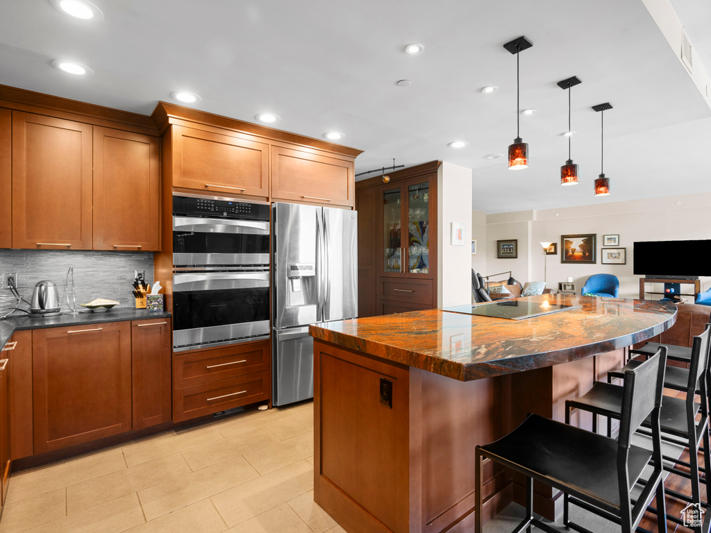 Kitchen with stainless steel appliances, a center island, open floor plan, brown cabinetry, and a kitchen bar