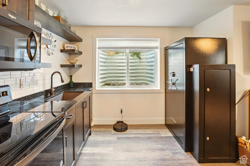 Kitchen featuring stainless steel appliances, a sink, light wood-type flooring, decorative backsplash, and open shelves