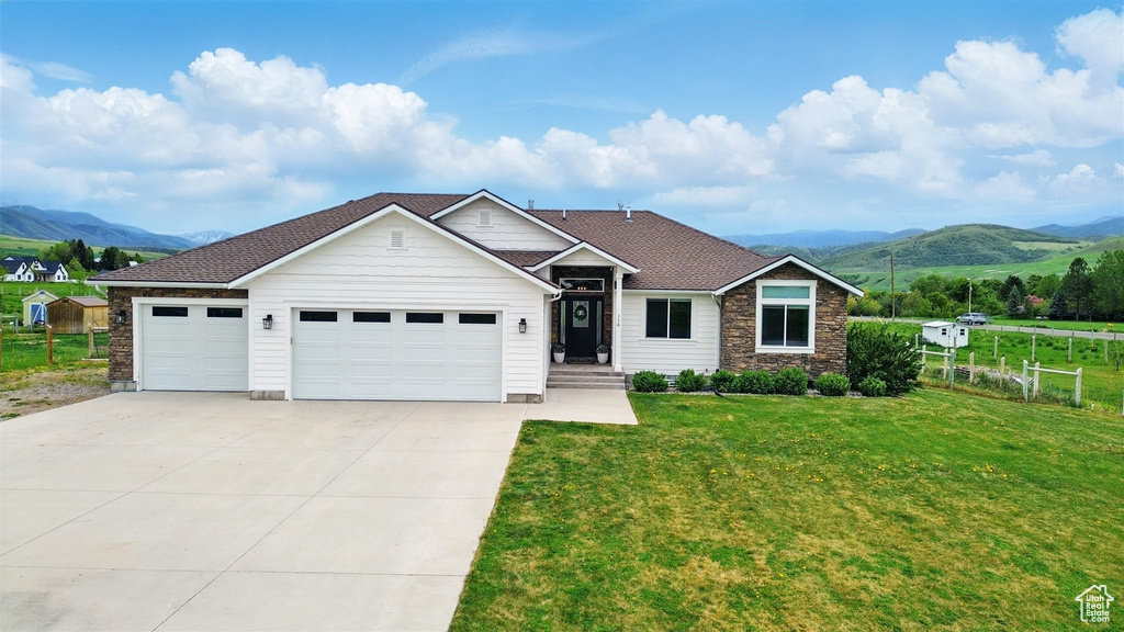 View of front of property with a mountain view, concrete driveway, a garage, stone siding, and roof with shingles