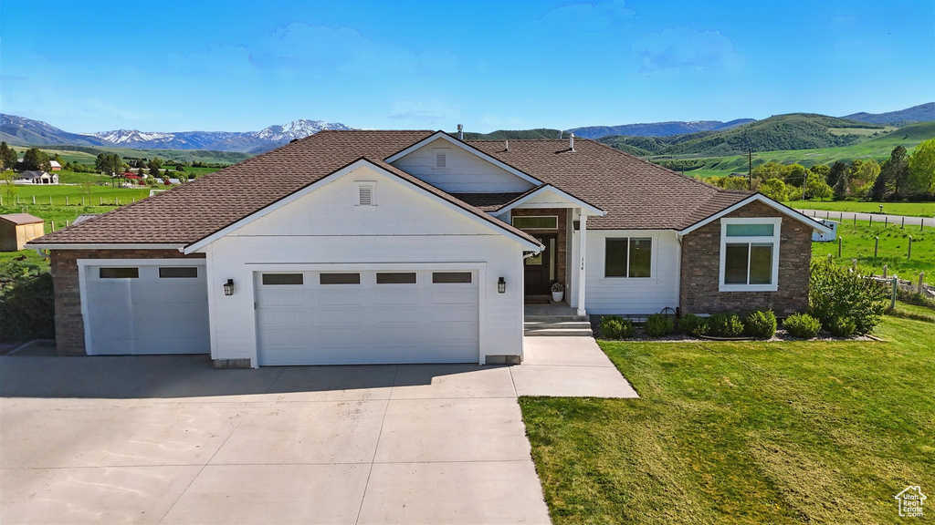 View of front of home with a mountain view, an attached garage, a front lawn, and driveway