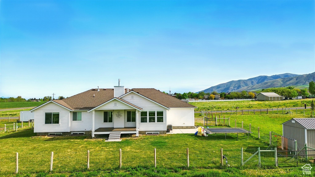 Back of house with a mountain view, a chimney, a shingled roof, a rural view, and an outdoor structure