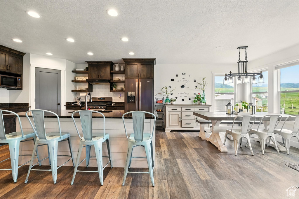 Kitchen featuring stainless steel appliances, open shelves, dark brown cabinets, dark countertops, and dark wood finished floors