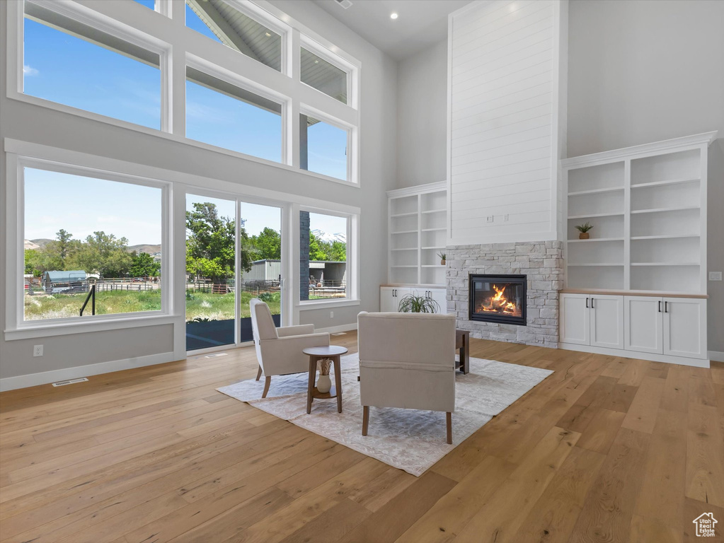 Living room featuring a high ceiling, a fireplace, light wood-style flooring, and baseboards
