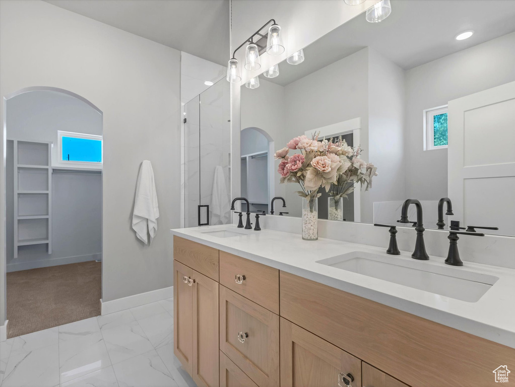 Full bathroom featuring double vanity, a shower with shower door, marble look tiles, baseboards, and a spacious closet