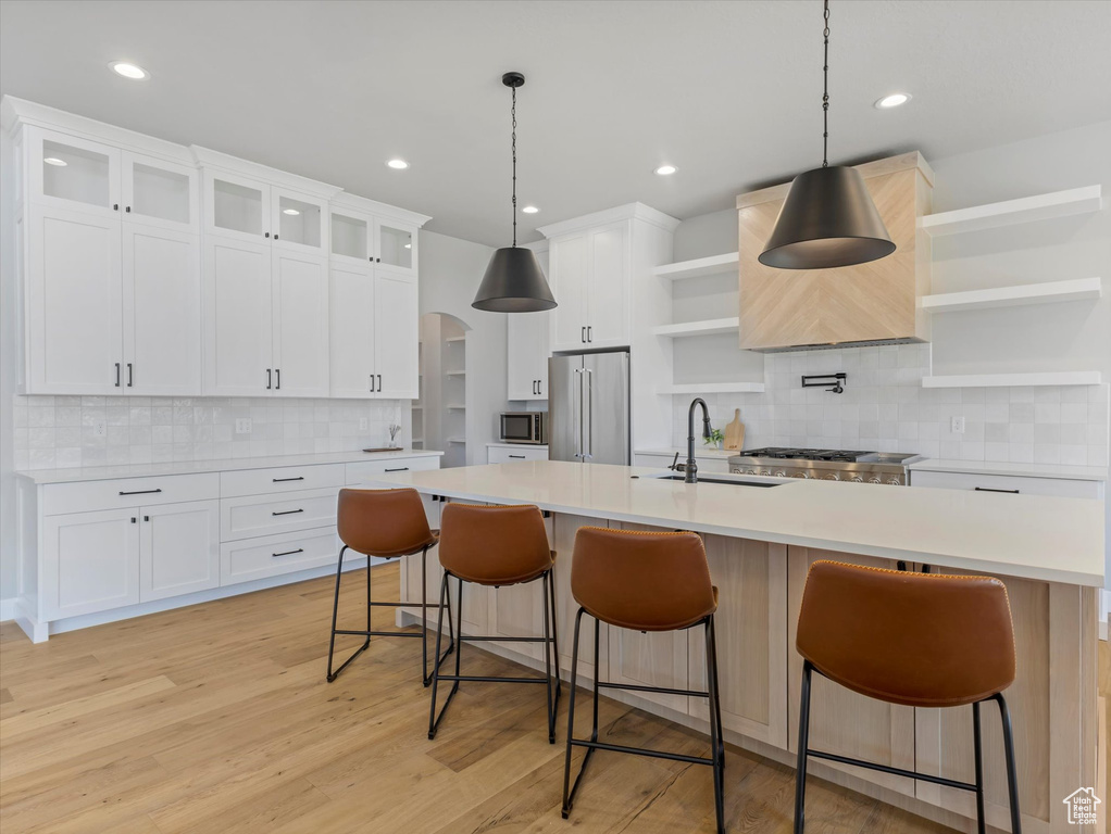 Kitchen featuring open shelves, appliances with stainless steel finishes, a sink, a center island with sink, and tasteful backsplash