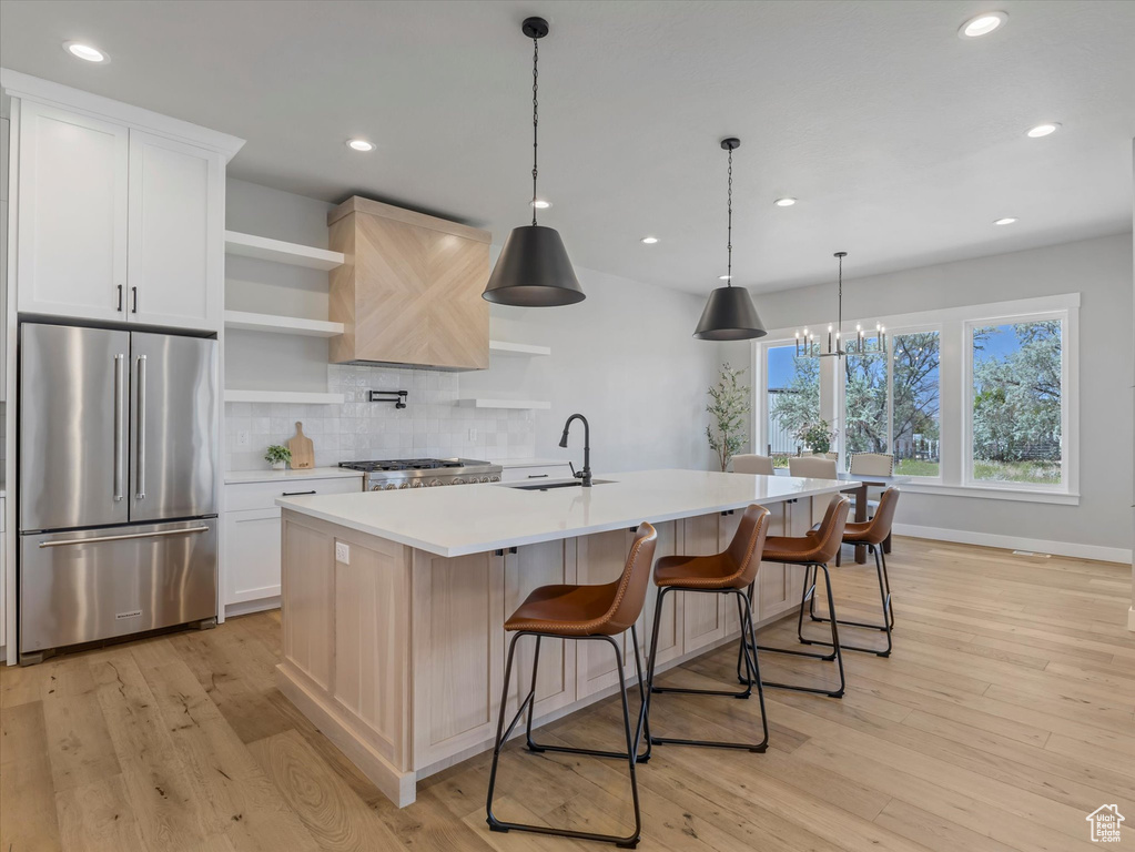 Kitchen featuring high quality fridge, a sink, open shelves, light countertops, and light wood-style floors