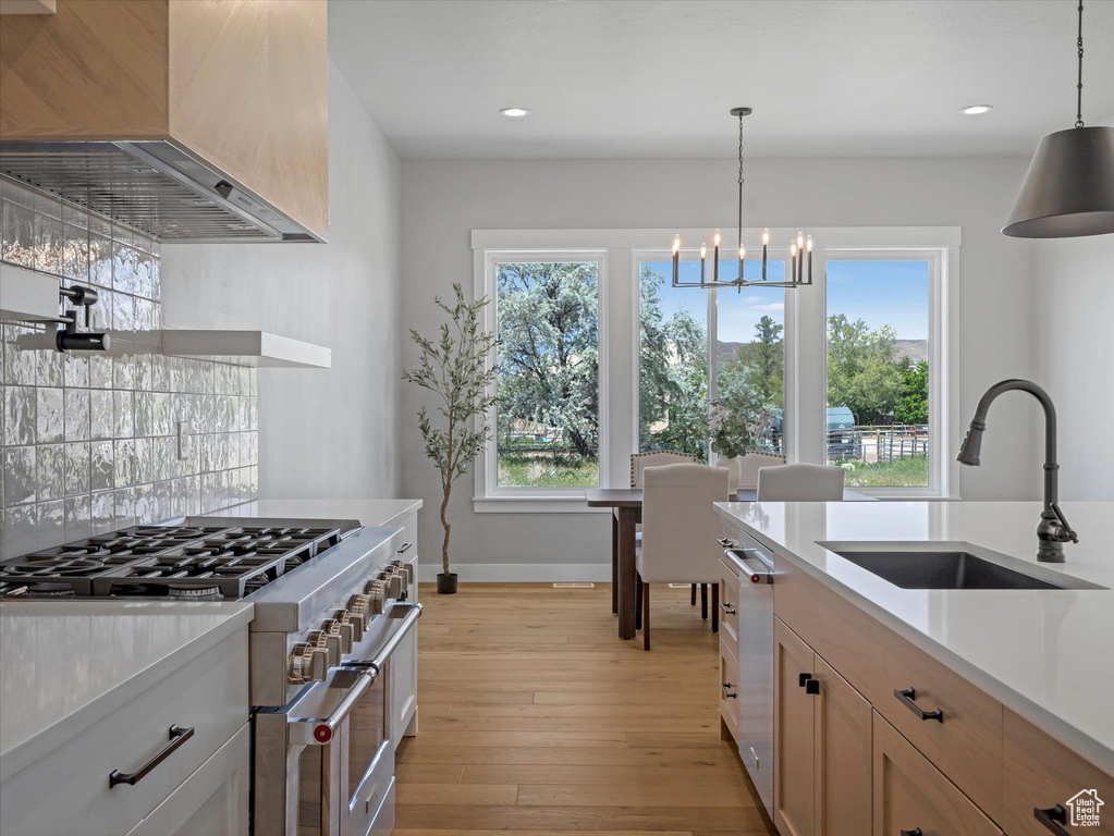 Kitchen featuring stainless steel appliances, a sink, wall chimney exhaust hood, light countertops, and a chandelier