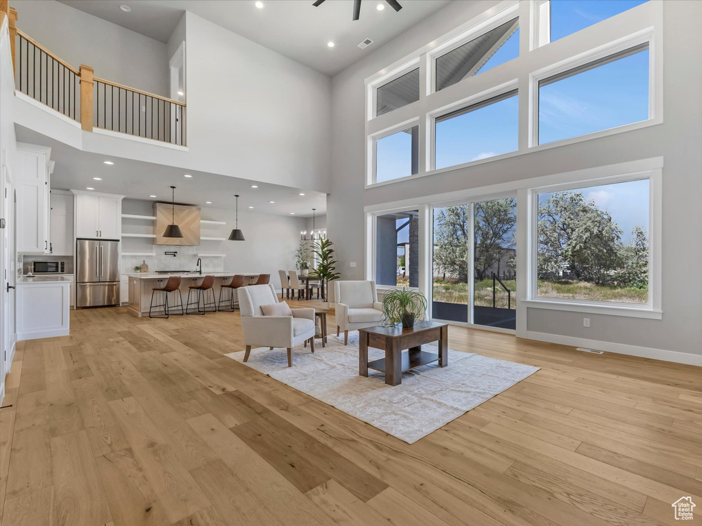 Living room featuring a high ceiling, light wood-style floors, baseboards, a ceiling fan, and recessed lighting