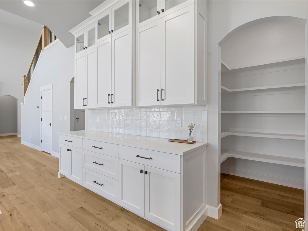 Kitchen featuring arched walkways, light countertops, light wood-type flooring, white cabinetry, and backsplash