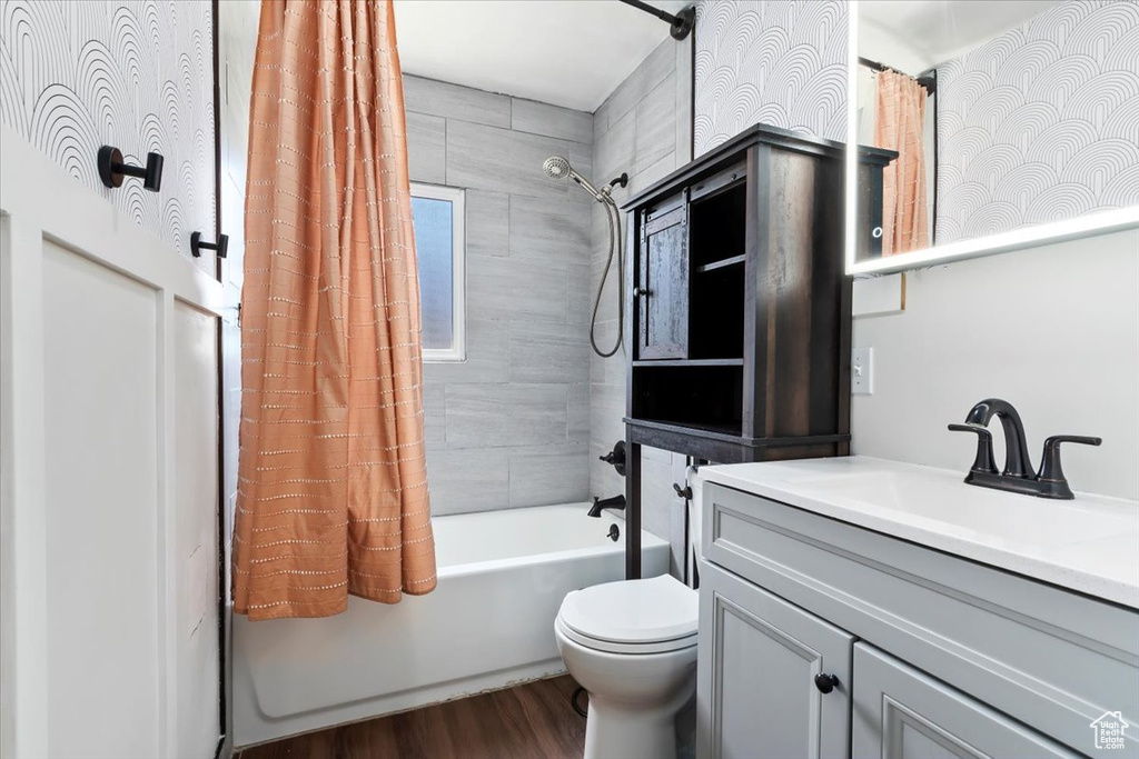 Full bathroom with wood finished floors, shower / bath combo with shower curtain, toilet, and vanity