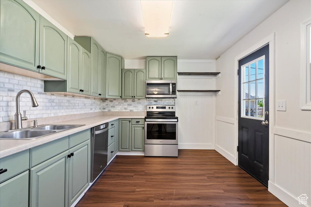 Kitchen with green cabinets, stainless steel appliances, a sink, open shelves, and tasteful backsplash