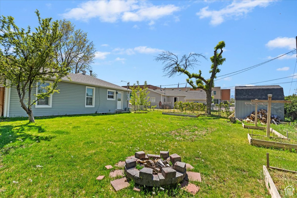 View of yard featuring a vegetable garden, a fire pit, an outbuilding, and a storage shed
