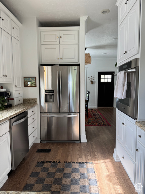 Kitchen featuring stainless steel appliances, dark wood-style flooring, white cabinets, and light stone countertops