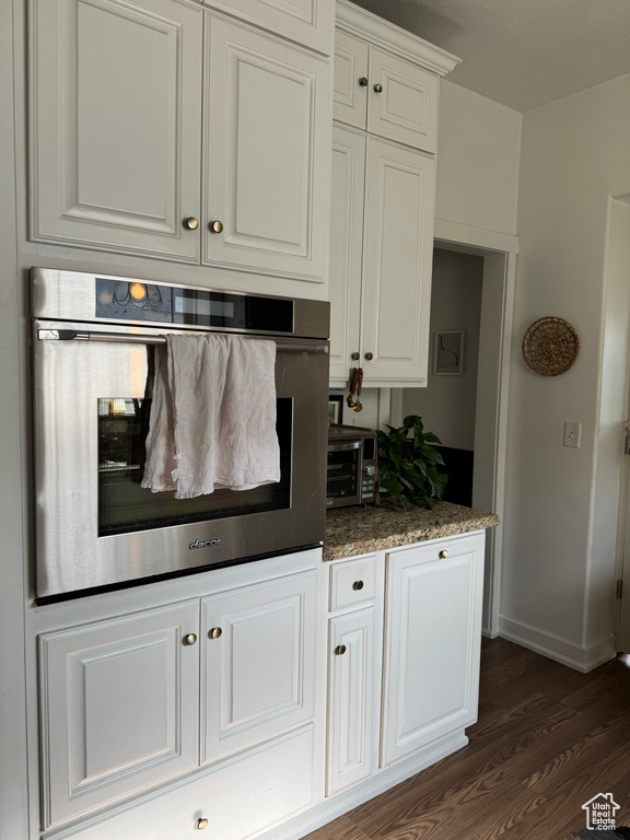 Kitchen with stainless steel oven, dark wood-type flooring, white cabinetry, and baseboards