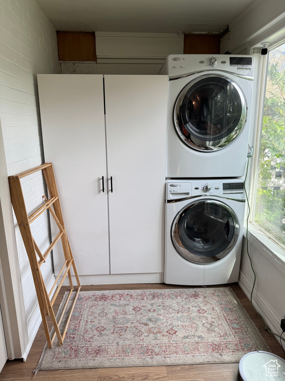 Laundry area with stacked washing machine and dryer and wood finished floors