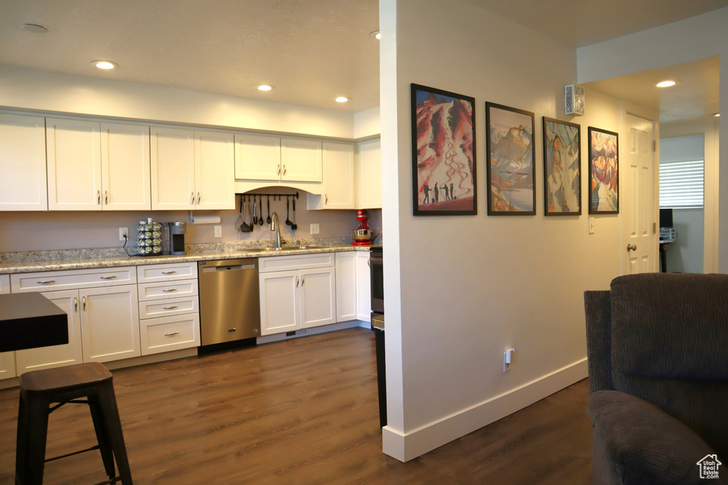Kitchen with stainless steel dishwasher, dark wood-type flooring, white cabinetry, baseboards, and recessed lighting