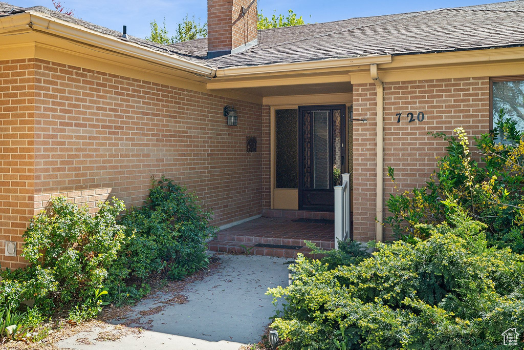 Property entrance featuring brick siding, a chimney, and a shingled roof