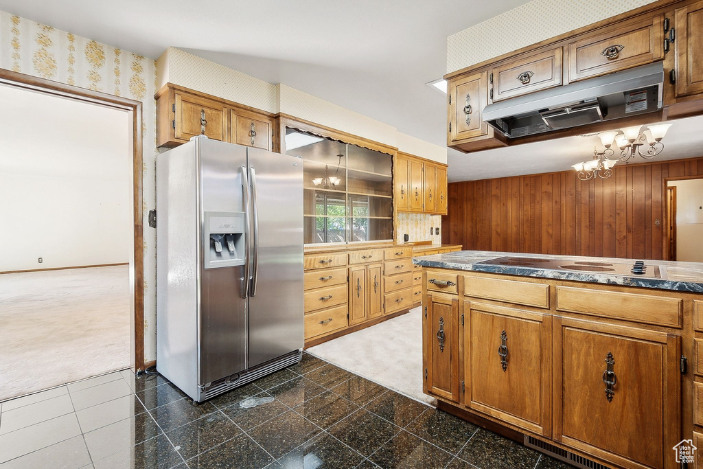 Kitchen with stainless steel refrigerator with ice dispenser, electric cooktop, a chandelier, dark carpet, and wood walls