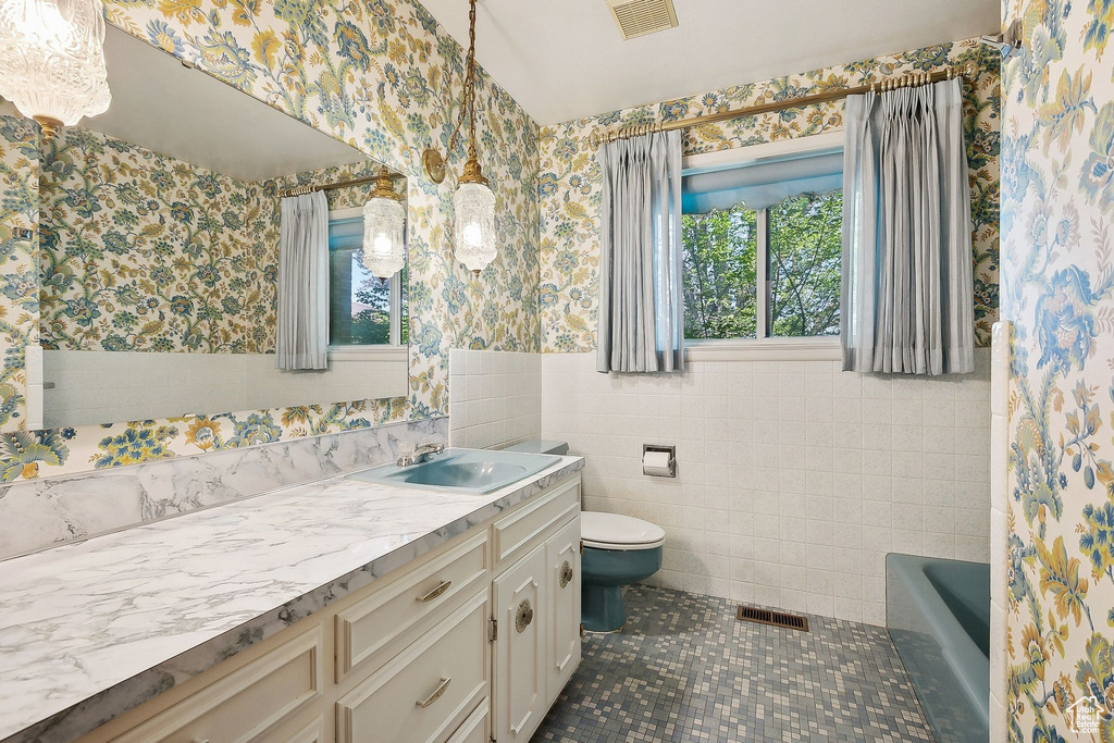 Full bath with wallpapered walls, toilet, wainscoting, vanity, and tile patterned floors